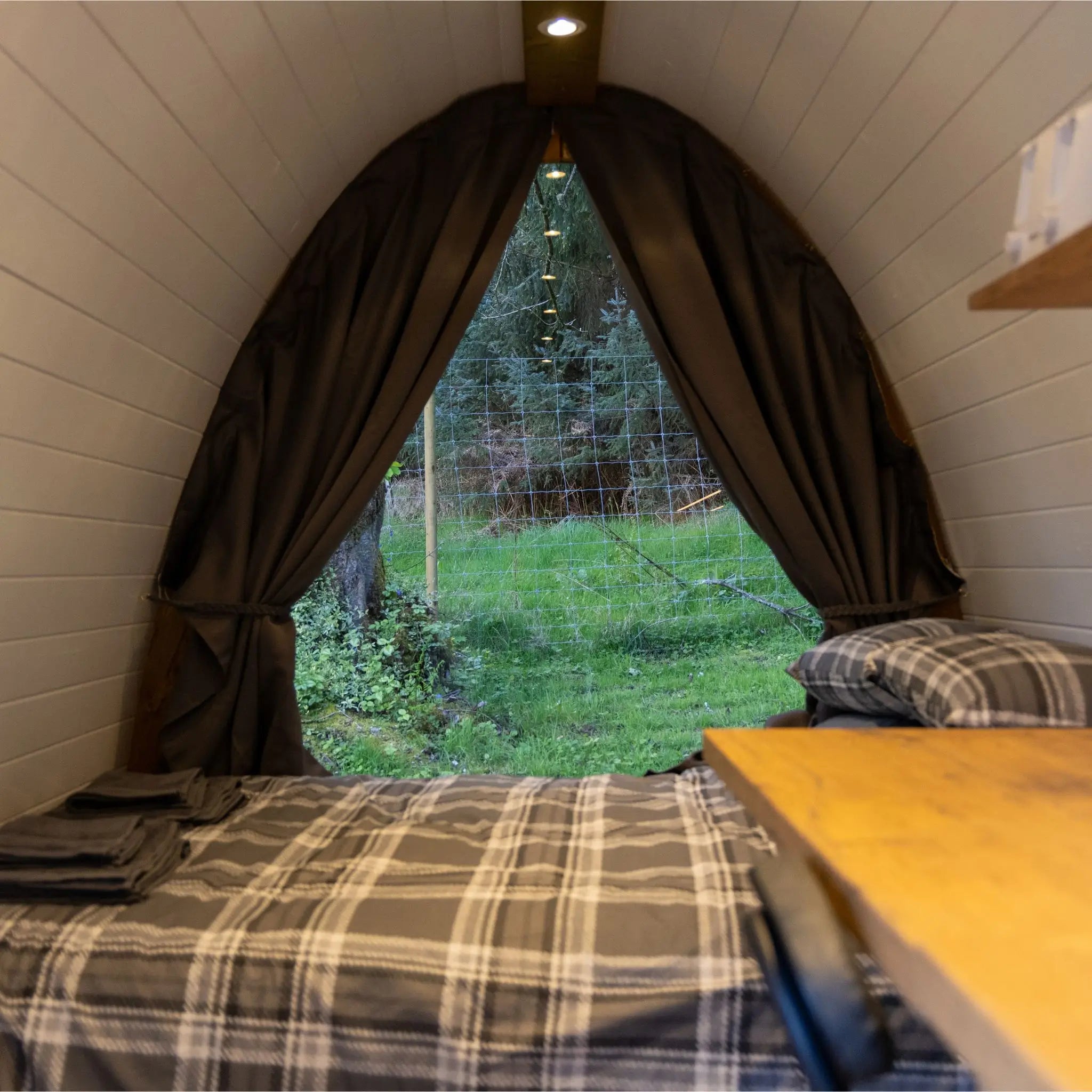 Bedroom with a large window showing greenery outside, plaid bedding, and wooden headboard.