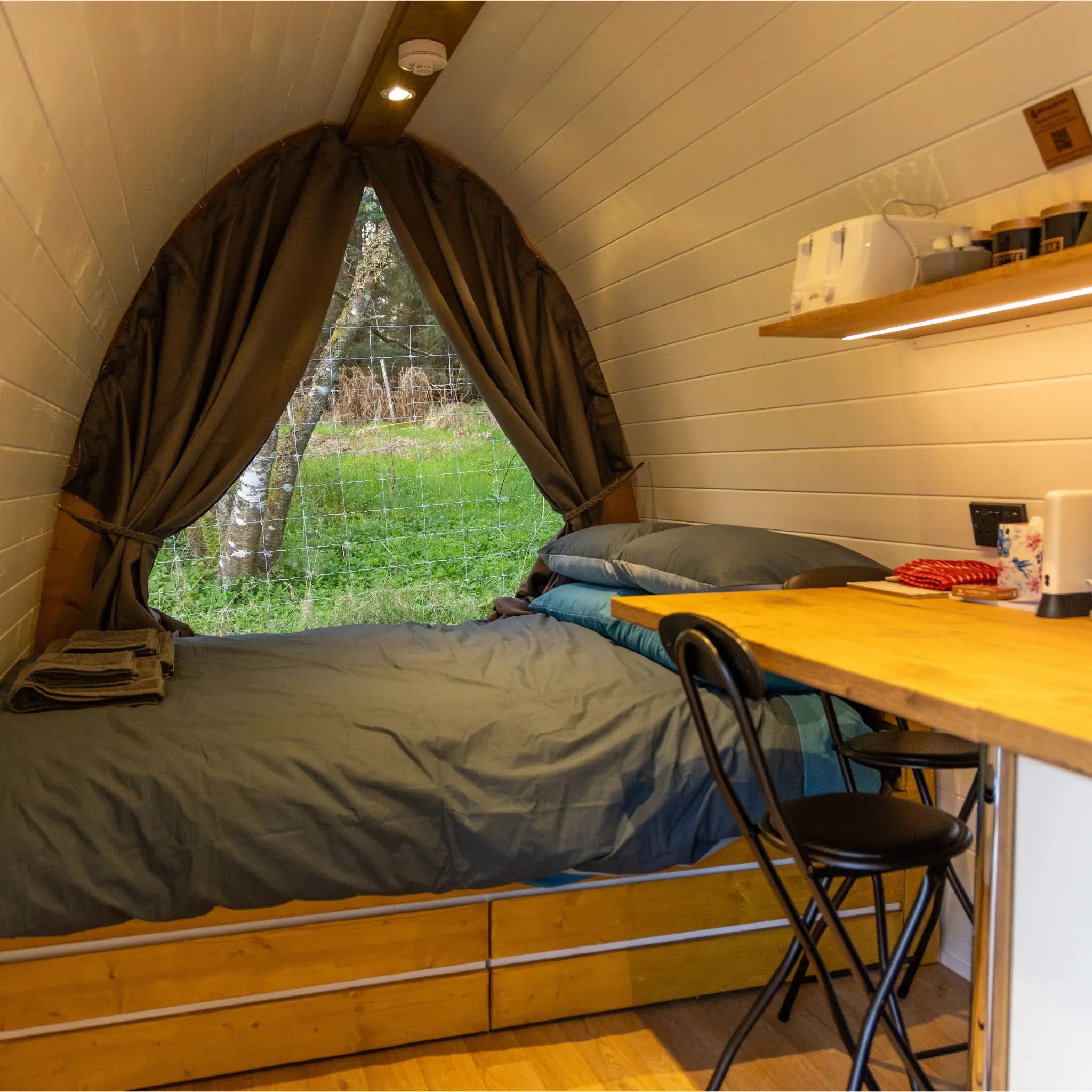 Small bedroom with bed, desk, and window view of greenery